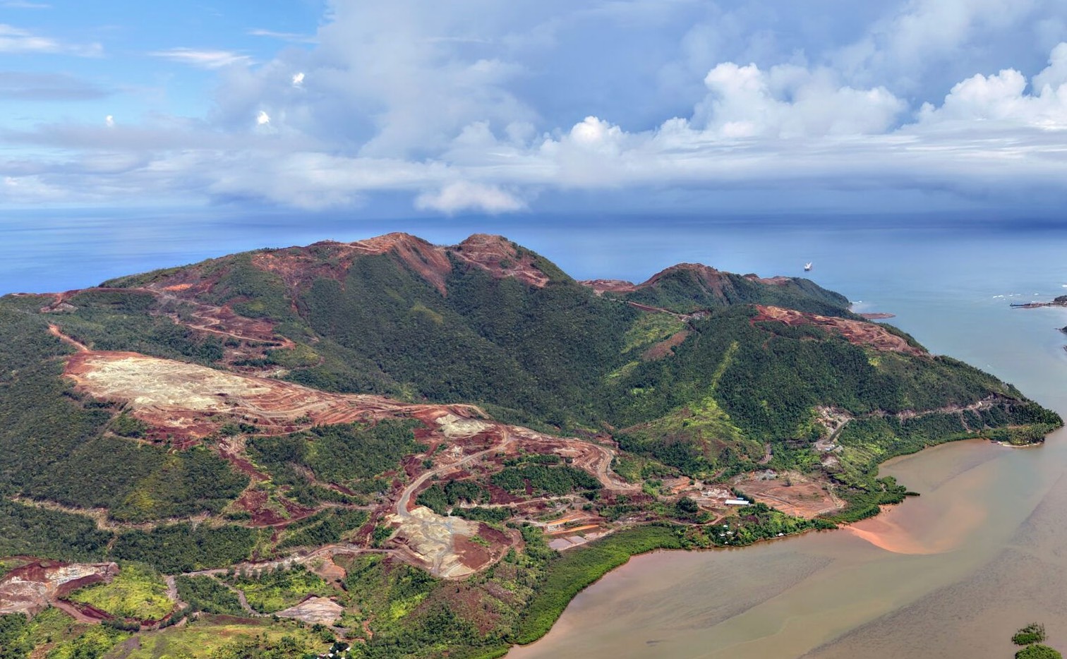 Aerial view of a Caraga coastline with red-brown siltation plume running from mine-stripped hillsides into the bay