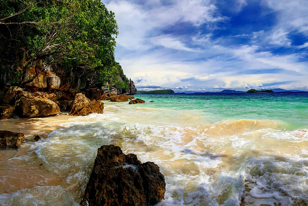 A beach and clear turquoise water in the Dinagat Islands, a coastline flanked by forested rocks